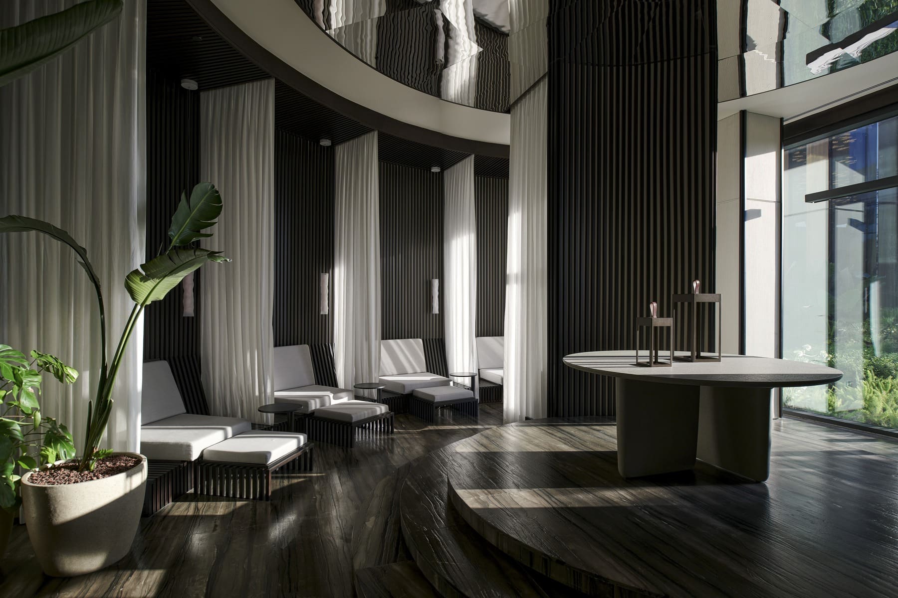 Modern lounge with dark vertical panels, white curtains, and white cushioned seating around small tables; large round table on a raised platform.