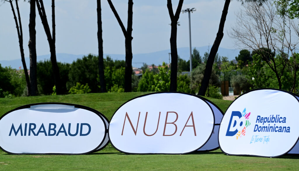 Row of white banner signs on a grassy field displaying 'MIRABAUD', 'INUBA', and 'República Dominicana' logos with trees in the background.