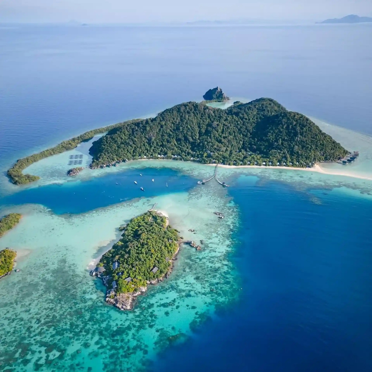 Tropical islands with turquoise water beside a forested shore.