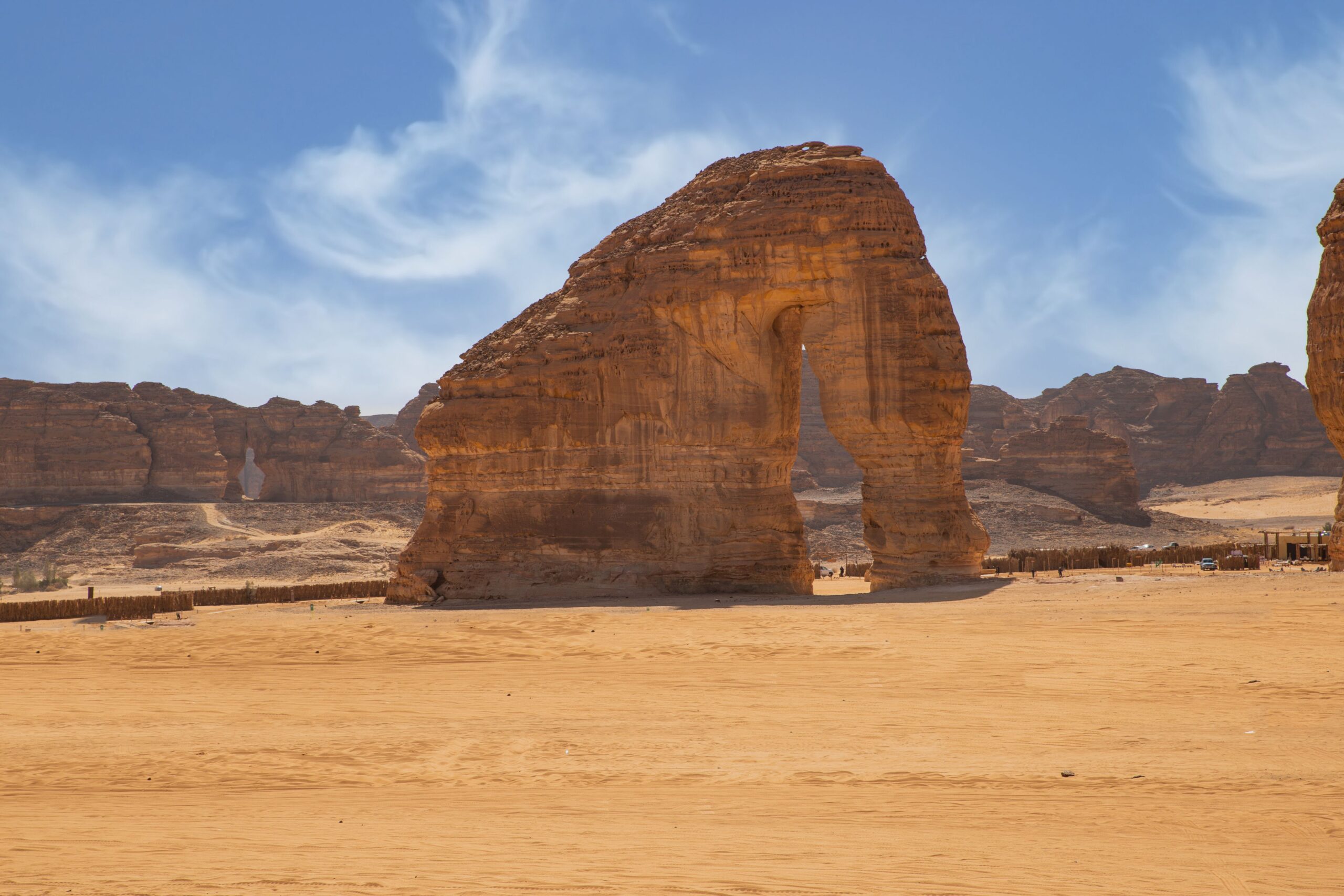 Desert landscape with a large sandstone arch centered under a blue sky.