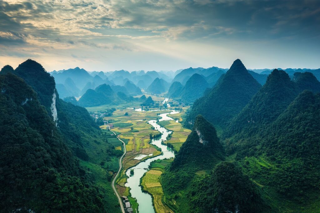 Winding river through terraced fields, surrounded by tall karst mountains under a cloudy sky