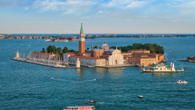 Aerial view of San Giorgio Maggiore with its tall bell tower and church, red-tiled buildings, and boats docked along the lagoon.